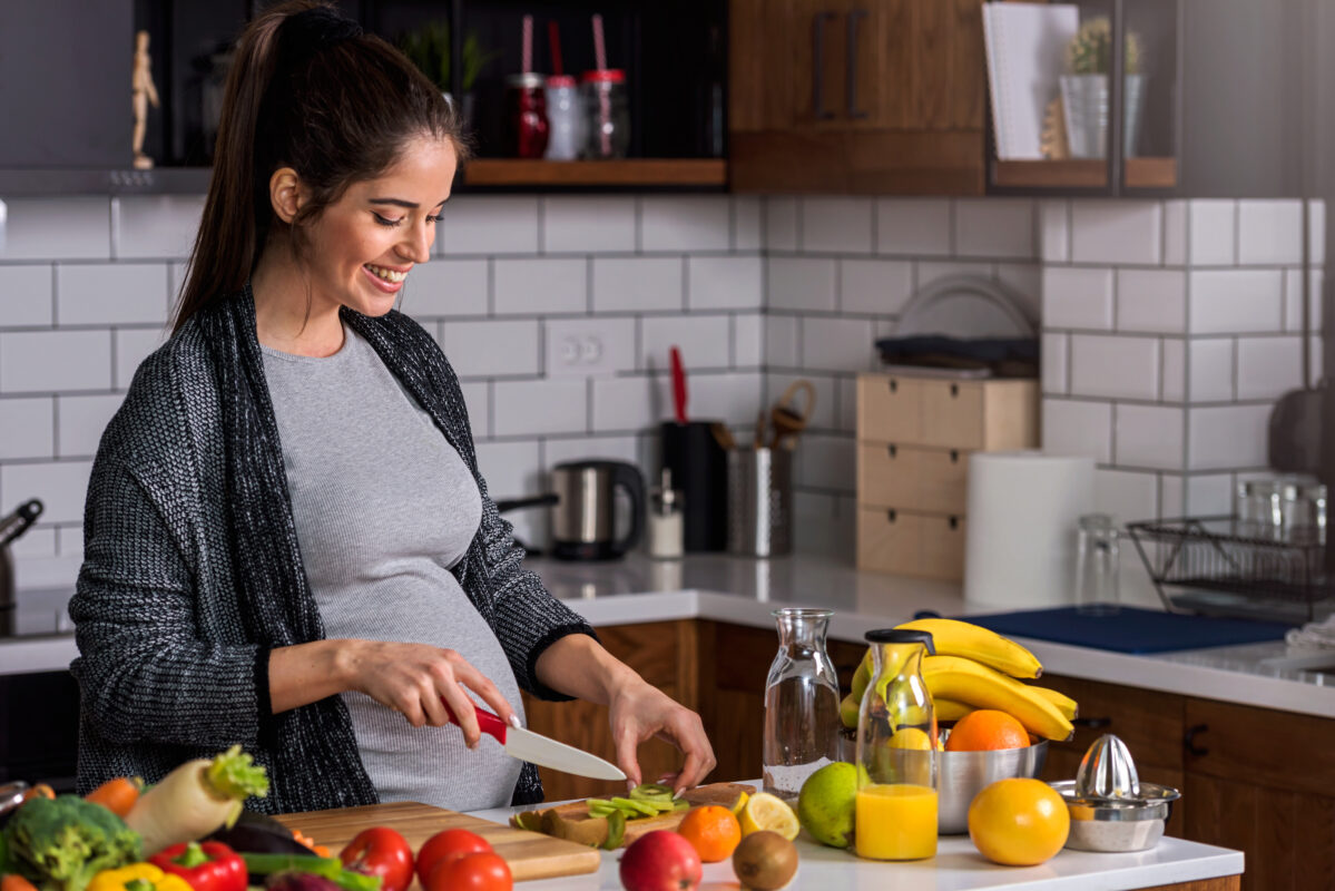 Smiling young pregnant woman preparing healthy food at home